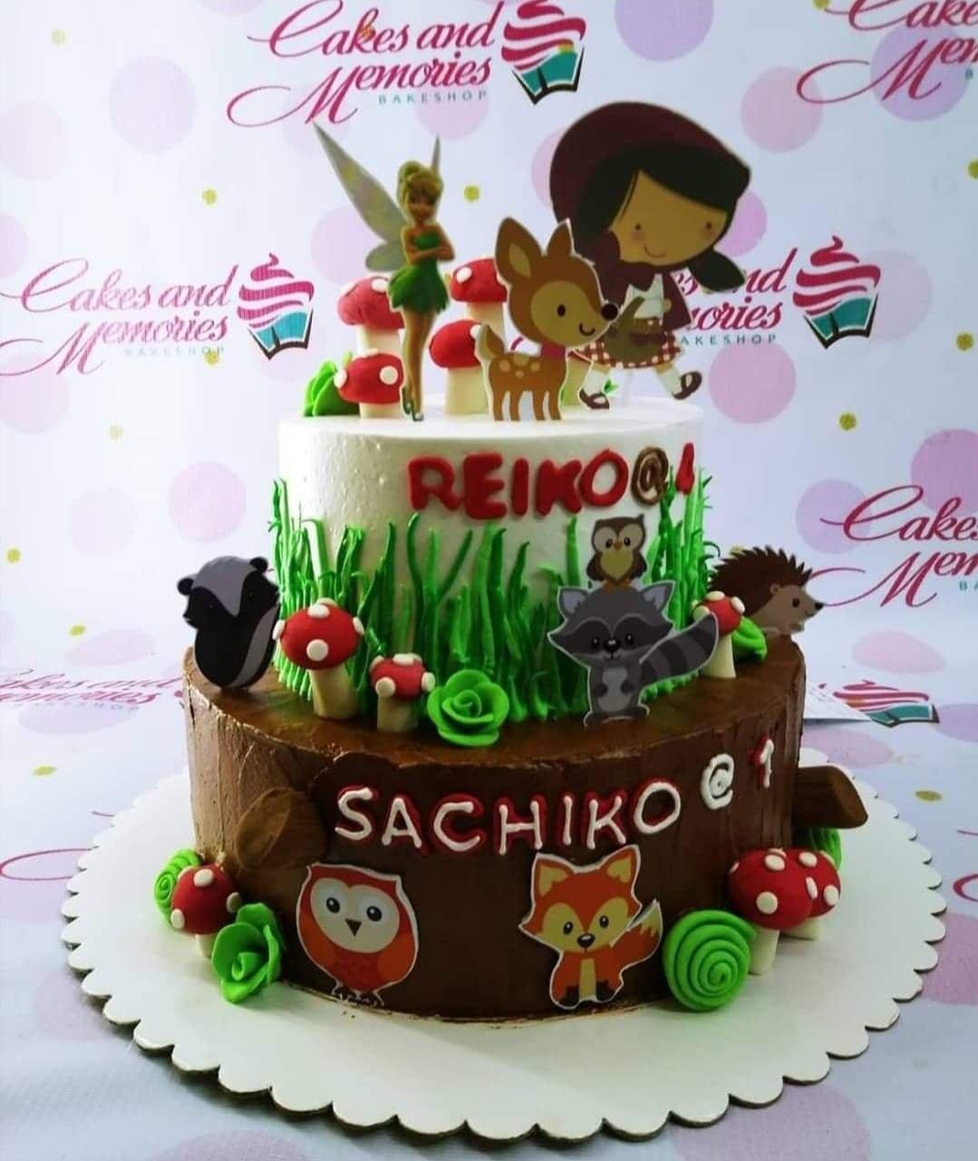 Two-tier woodland and fairy themed cake with brown and white icing, featuring forest animals, mushrooms, and a Tinkerbell topper.