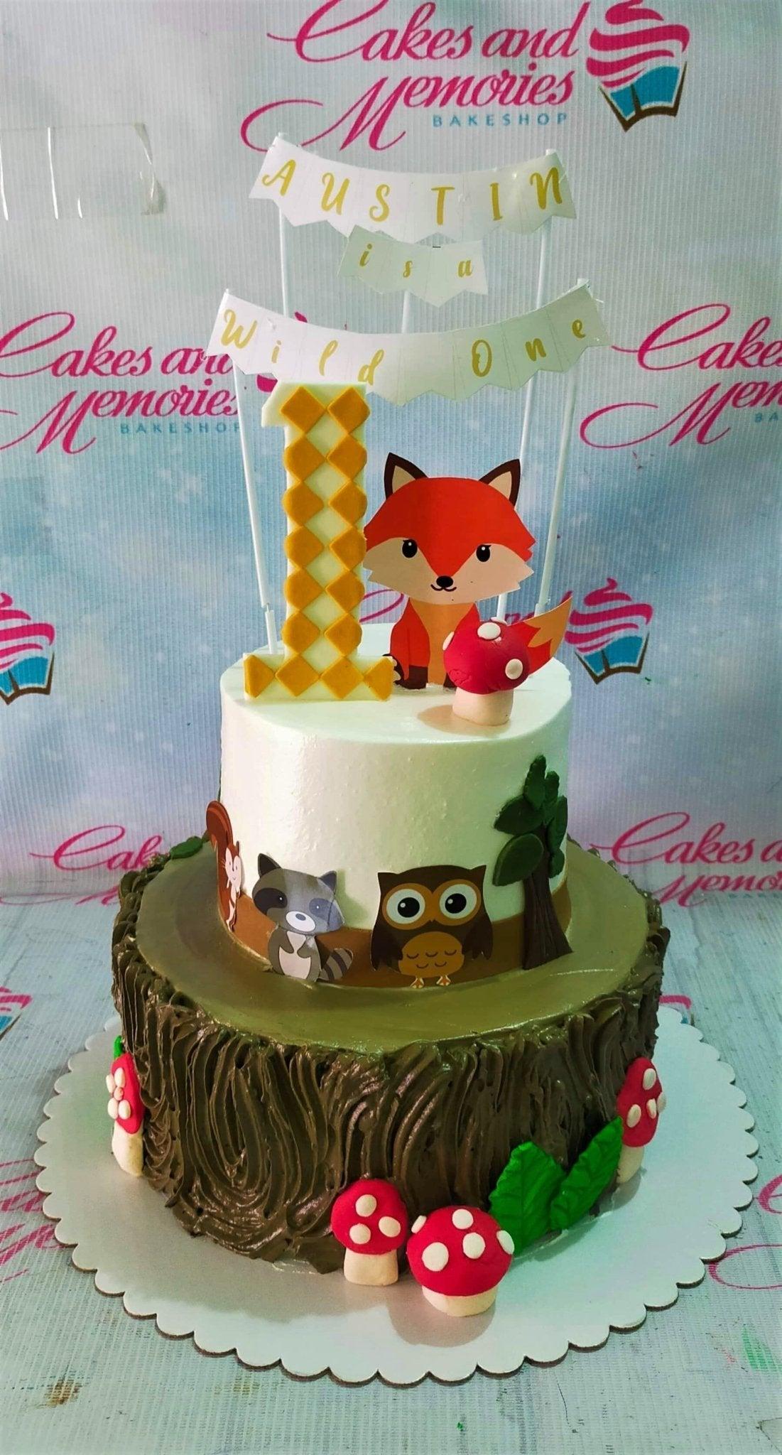 Two-tier woodland themed birthday cake with a fox topper, forest animal printouts, and red fondant mushrooms on a tree bark textured base.