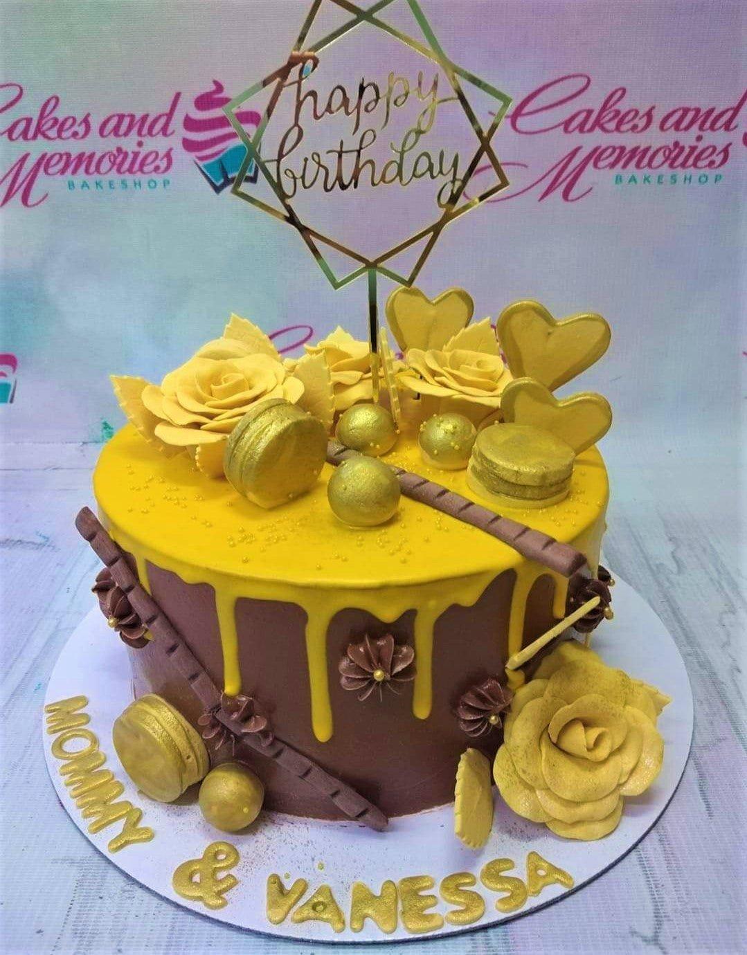 Brown and yellow chocolate drip cake with gold macarons, roses, and a Happy Birthday topper for Mommy and Vanessa.