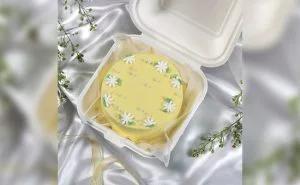 Yellow bento cake with white icing daisies and green leaves in a white takeout box