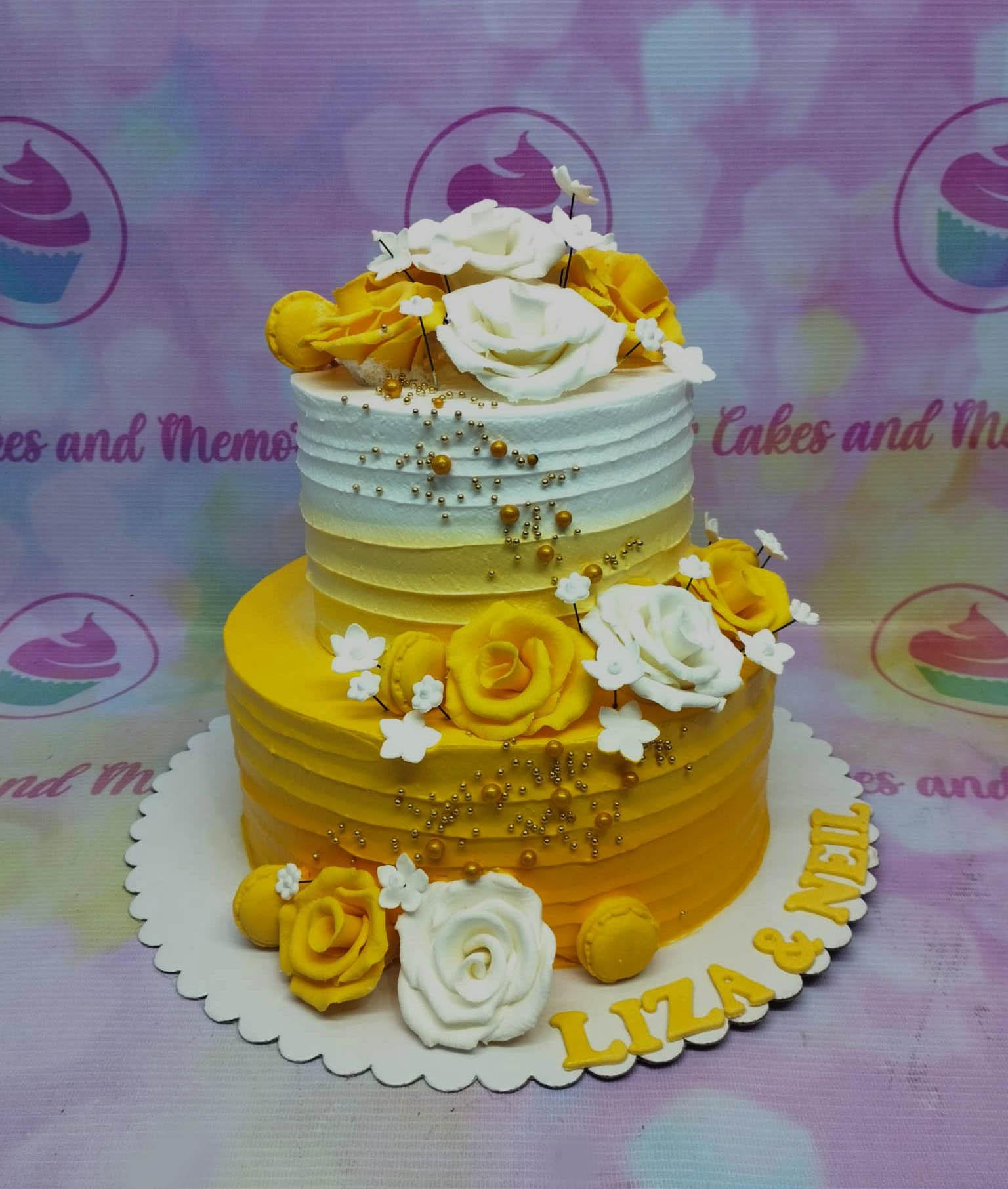 Two-tier yellow and white ombre cake decorated with yellow and white gumpaste roses, gold dragees, and yellow macarons.