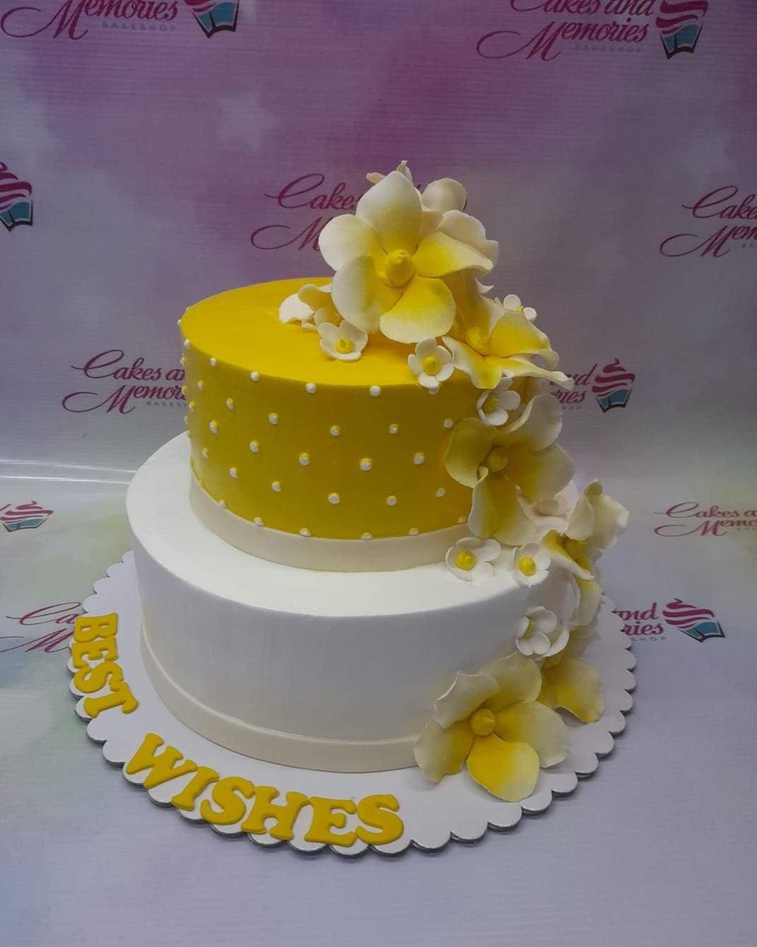 Two-tier yellow and white fondant cake decorated with cascading yellow and white gumpaste flowers and white polka dots.