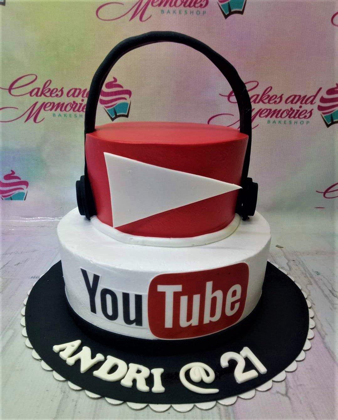 Two-tier YouTube themed cake with a red top tier featuring a white play button and a white bottom tier with the YouTube logo and headphones.