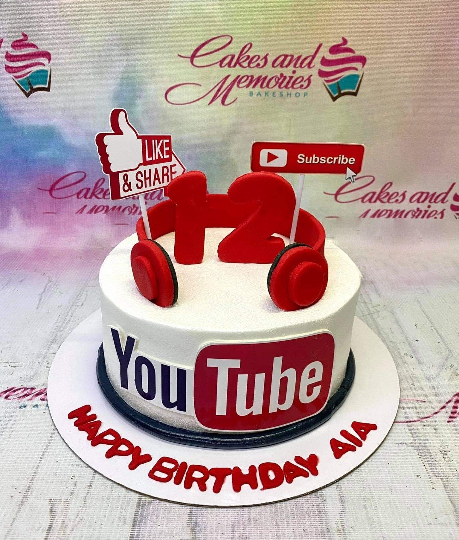 YouTube themed birthday cake with red headphones, Like and Share sign, Subscribe button, and a large YouTube logo on white icing.