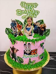 Pink Zootopia themed birthday cake with green icing grass, character printouts, and a personalized photo topper for Ana's 8th birthday.