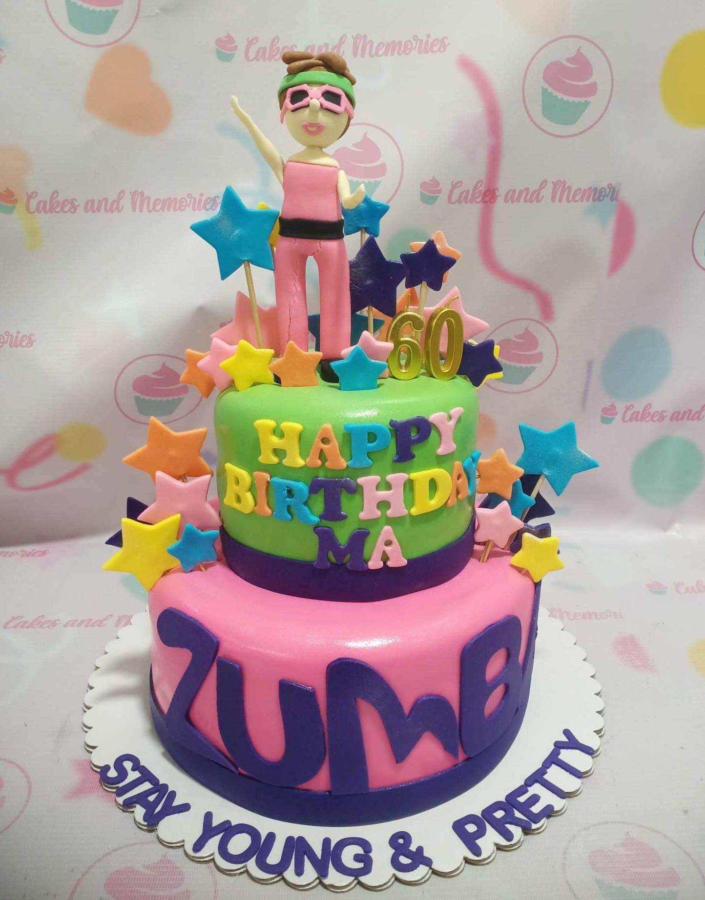 Two-tier Zumba themed birthday cake in pink and green with a fondant woman figure, colorful stars, and a gold 60 topper.