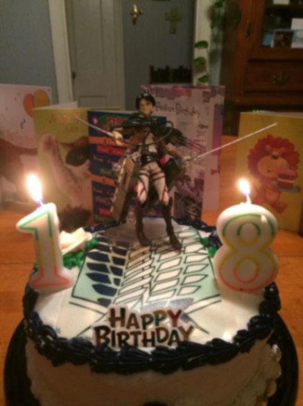 Attack on Titan themed birthday cake with Levi Ackerman figure, number 18 candles, and Wings of Freedom logo.