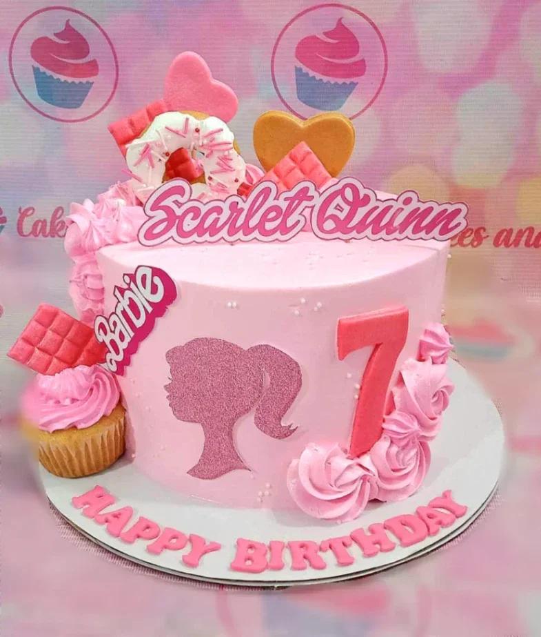 Pink Barbie themed birthday cake with a glittery silhouette, pink chocolate bars, a donut, and pink icing rosettes.