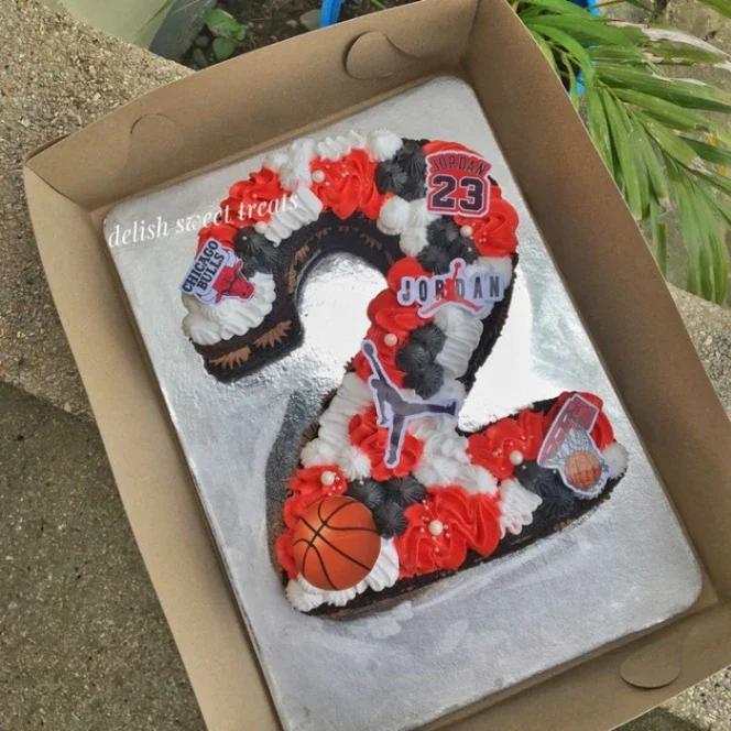 Number 2 shaped chocolate cake with red, white, and black icing rosettes and Michael Jordan basketball themed printout toppers.