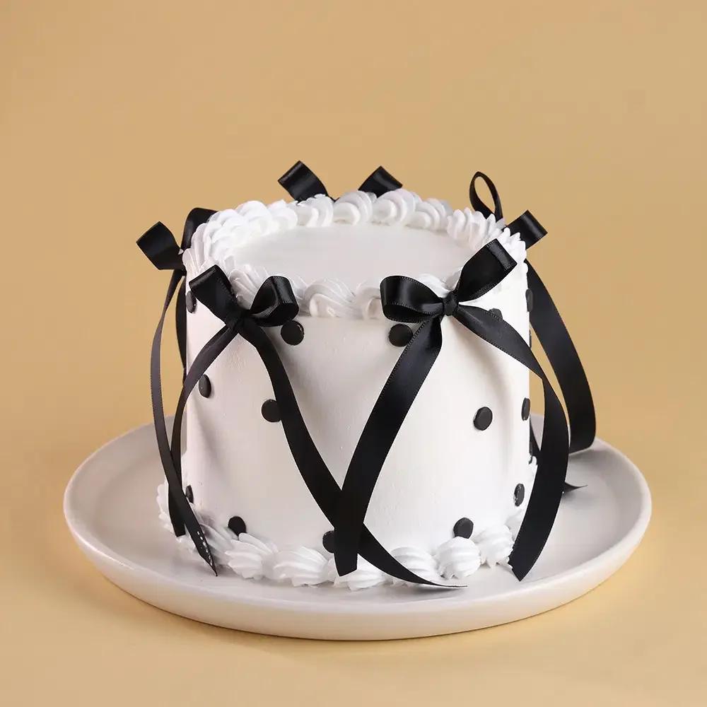 White minimalist cake with black satin bows and black polka dots on a white plate.