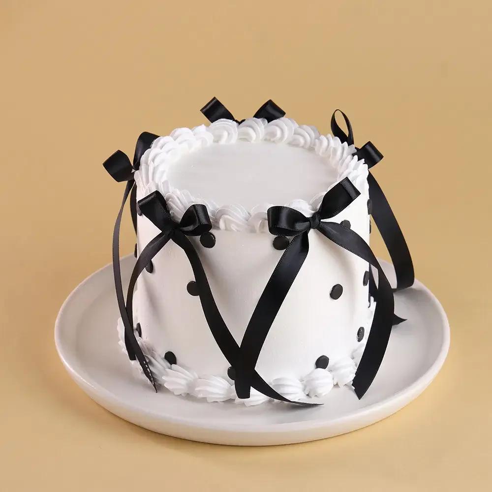 White minimalist cake with black satin bows and black polka dots on a white plate.