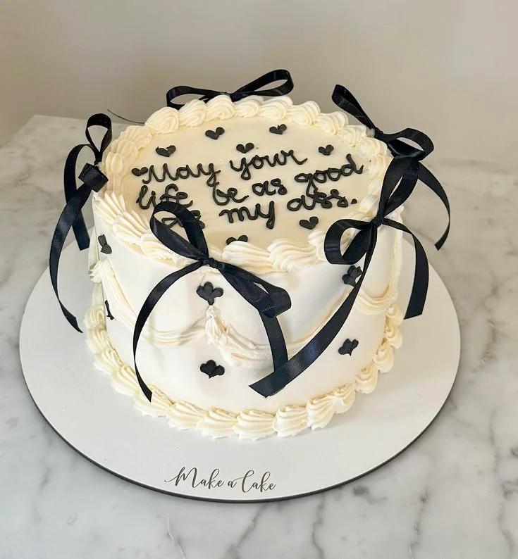 White minimalist cake with black piped message and black satin ribbons on a white base board.
