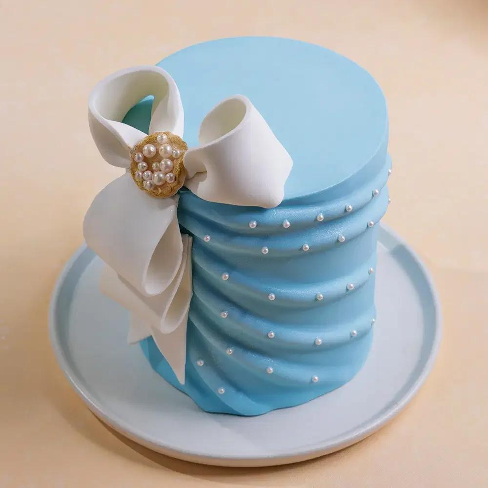 Tall light blue cake with elegant white fondant bow and pearl accents on a matching blue plate.