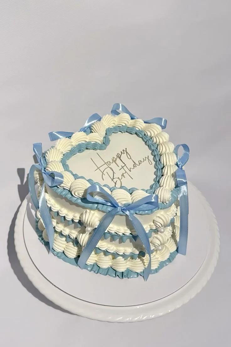 Heart-shaped vintage style cake with white and light blue ruffled icing borders and blue satin ribbons.