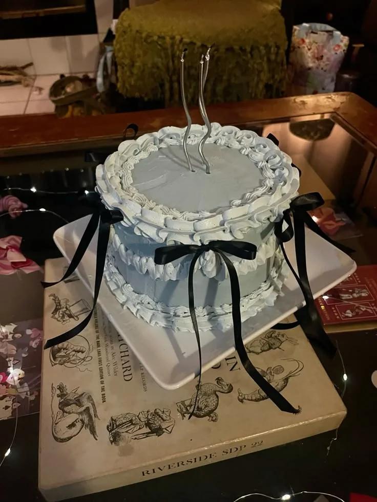 Light blue vintage style cake with ruffled icing borders and black satin ribbons on a white square plate.