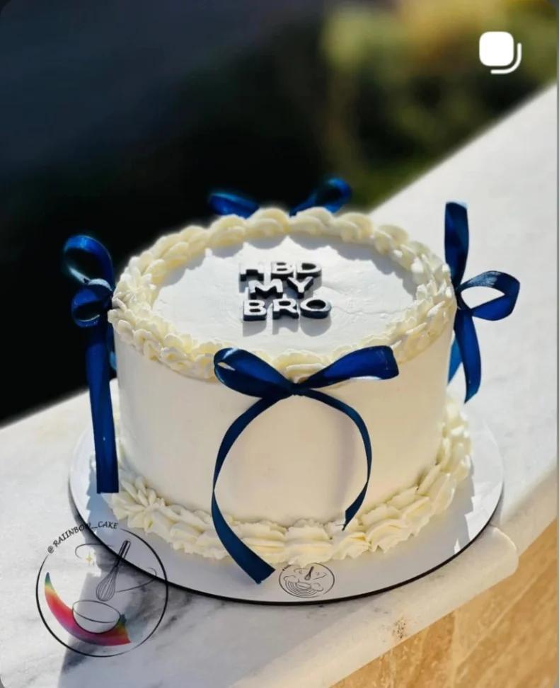 White minimalist cake with navy blue ribbons and black gumpaste letters reading HBD MY BRO.