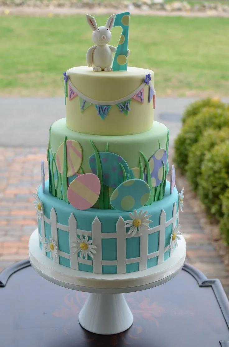3-tier pastel fondant birthday cake with a bunny topper, number 1, edible Easter eggs, and a white picket fence design.