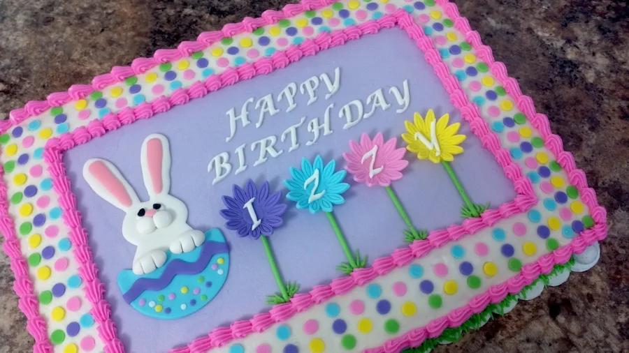Purple rectangular birthday cake for Izzy featuring a white fondant bunny in an Easter egg and colorful fondant flowers with letters.
