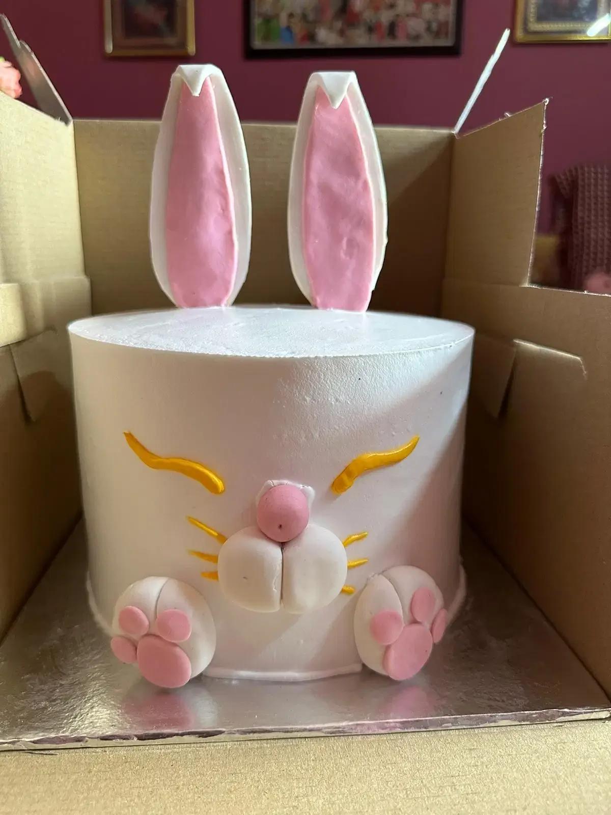 White bunny-themed cake with pink fondant ears, paws, and a cute face with yellow whiskers.