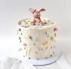 Cream colored single tier cake with a hand-sculpted brown bunny topper and delicate pastel piped icing flowers on the sides.