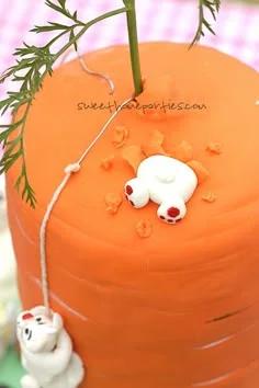 Tall orange carrot-shaped fondant cake with a white bunny digging into the top and another bunny climbing the side with a rope.