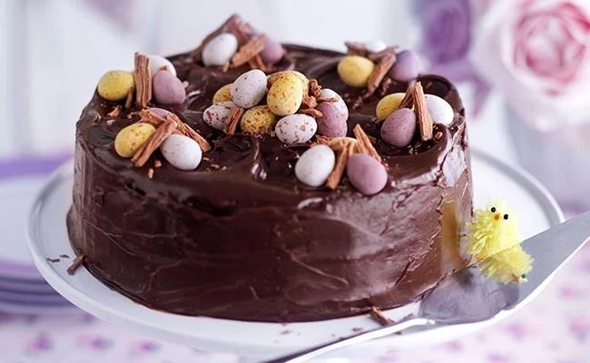 Rich chocolate cake with dark chocolate icing topped with colorful candy eggs and chocolate shavings.