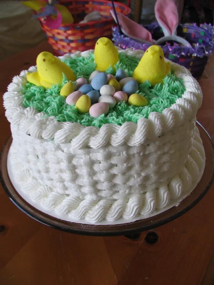 White basketweave icing cake topped with green grass icing, yellow marshmallow chicks, and pastel candy eggs.