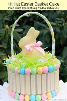 Kit Kat Easter basket cake with white chocolate bars, pastel candy eggs, green icing grass, and a yellow chocolate bunny topper with a pink bow.