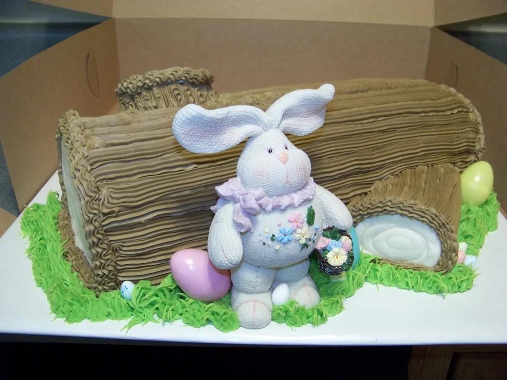 Easter log cake with a large white bunny figurine, colorful eggs, and green grass icing.