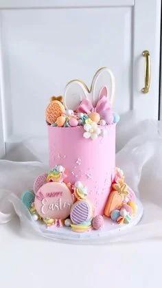 Tall pink Easter cake with bunny ears, fondant eggs, carrots, and a Happy Easter message on a pink cookie.