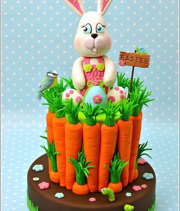 A tall brown fondant cake decorated with large orange fondant carrots, a large white bunny figure, a blue bird, and a wooden Easter sign.