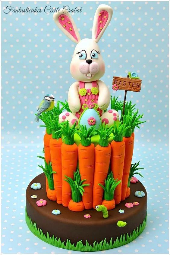 Easter bunny cake with fondant carrots, a blue bird, and a wooden sign topper on a brown base.