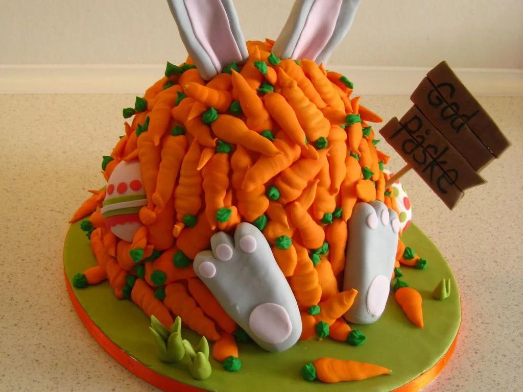 Easter bunny cake covered in orange fondant carrots with grey bunny feet and ears, and a wooden-style sign.