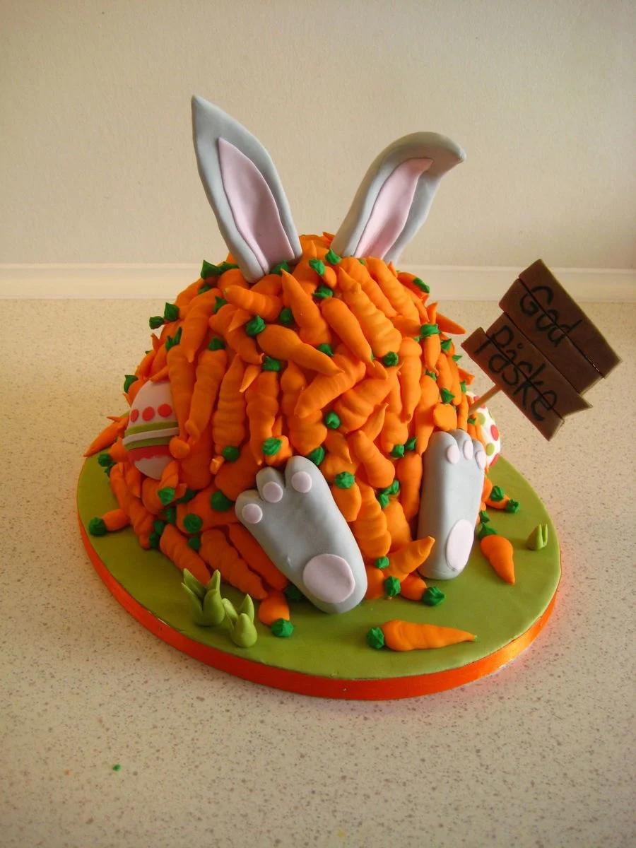 A whimsical Easter bunny cake covered in numerous orange fondant carrots with green tops, featuring bunny ears and feet on a green base.