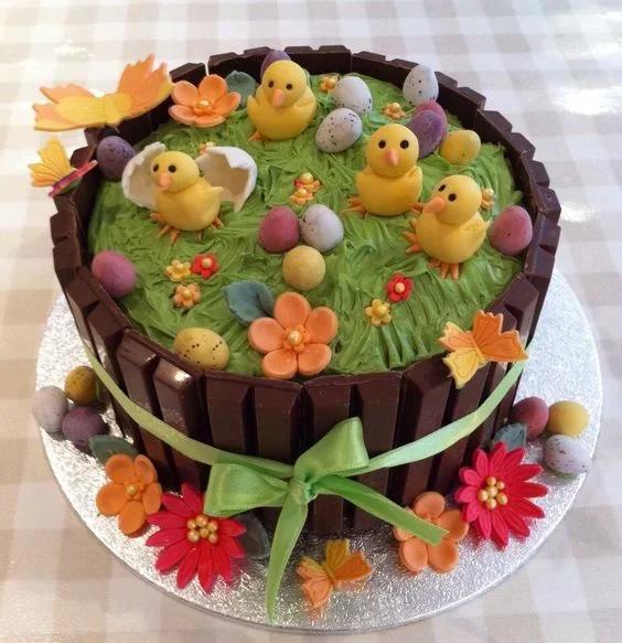 A round chocolate KitKat cake with green icing grass, yellow fondant chicks, and colorful Easter eggs.