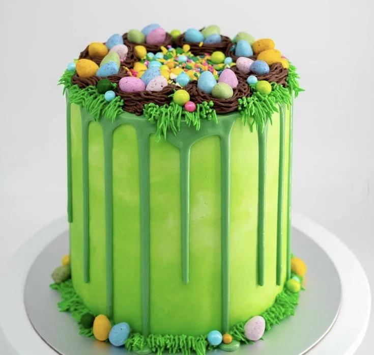 Tall light green drip cake with chocolate bird nests, colorful speckled eggs, and green icing grass for Easter.