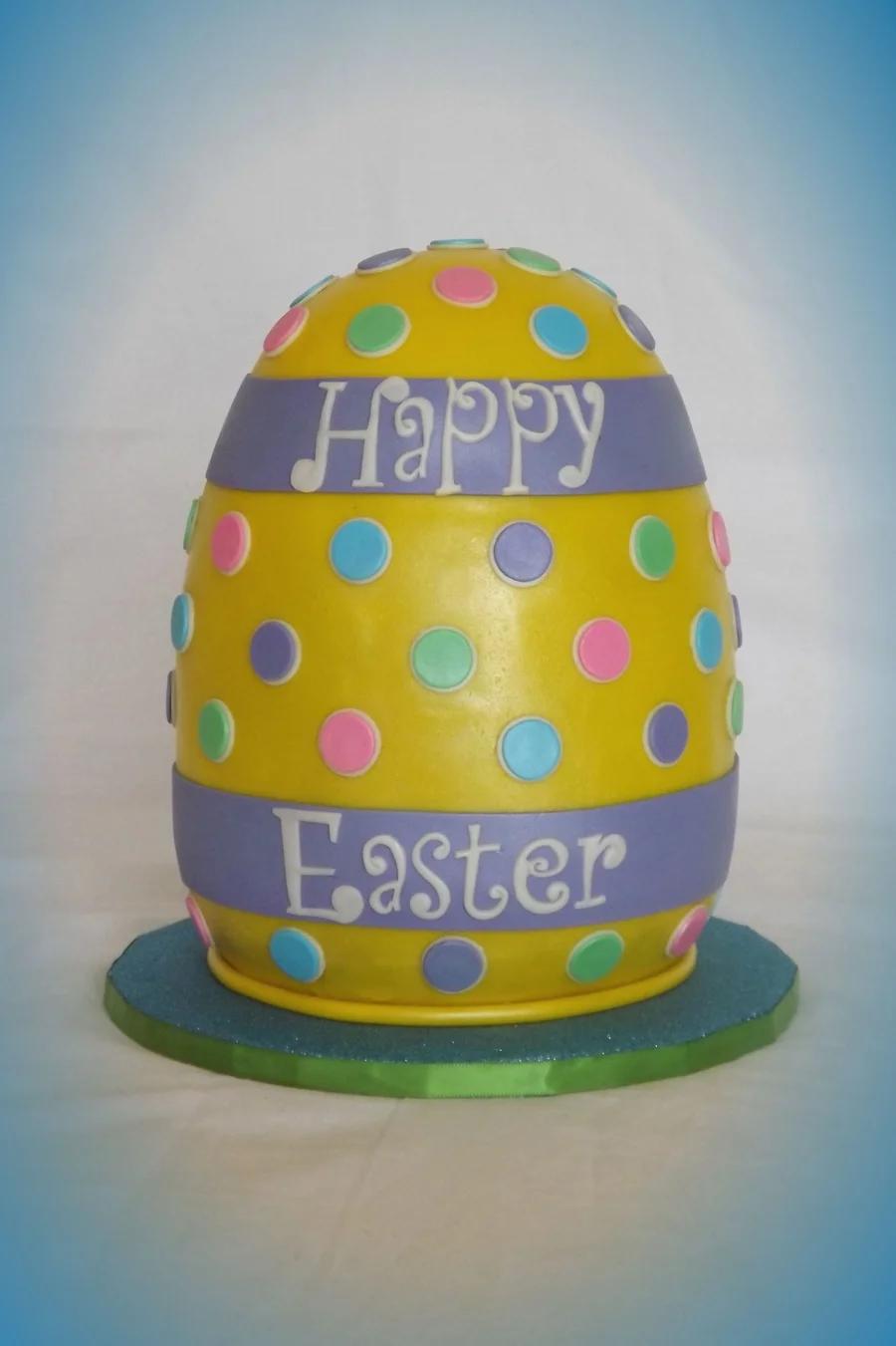 Yellow egg-shaped Easter cake with purple fondant bands and colorful polka dots on a green and blue base.