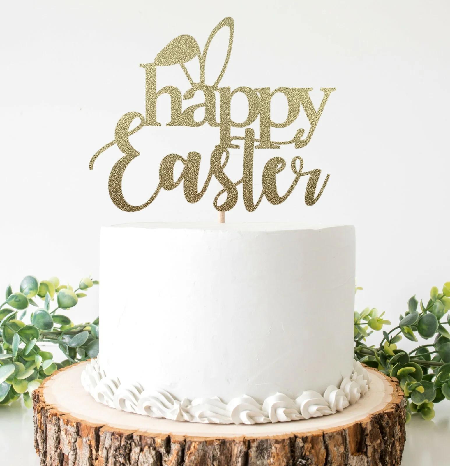 A minimalist white 1-tier cake with a gold glitter Happy Easter topper featuring bunny ears, displayed on a rustic wood slice base.