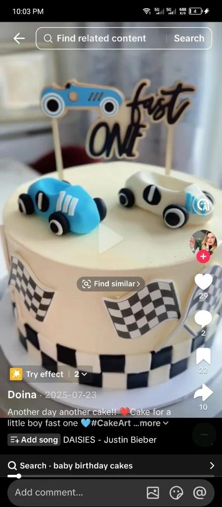 A light yellow single-tier birthday cake with a racing theme featuring blue and white toy cars and checkered flag decorations.