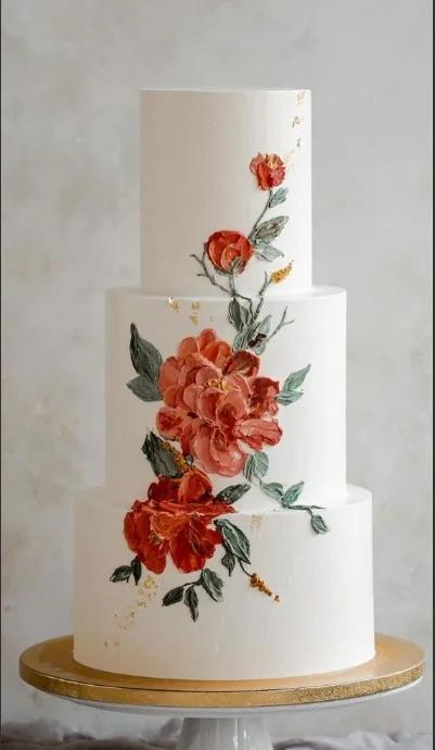 Elegant 3-tier white wedding cake featuring intricate orange and red palette knife floral icing decorations with gold leaf accents.