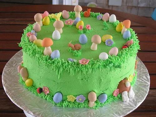 Green garden themed cake with fondant mushrooms, snails, flowers, and colorful eggs on a grass-textured icing base.