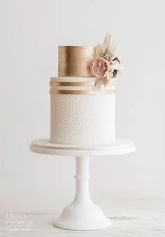 Elegant two-tier white fondant cake with a metallic gold top tier and delicate pink and ivory sugar flowers.