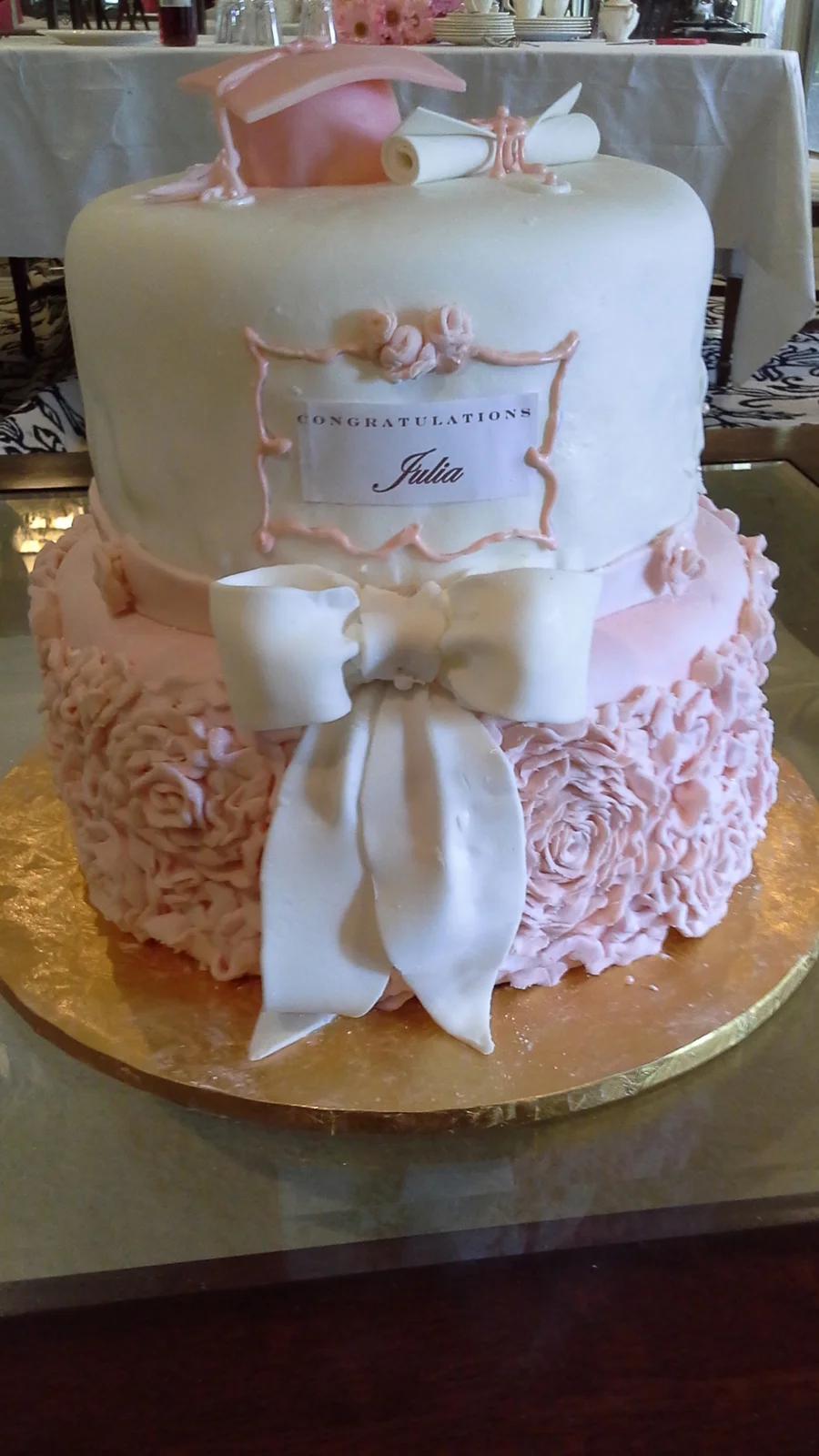 Elegant 2-tier white and pink graduation cake with a fondant graduation cap, scroll, and large white bow.