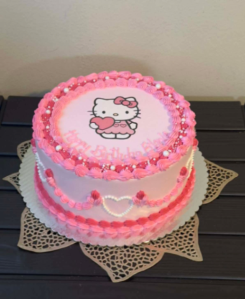 Pink Hello Kitty birthday cake with piped icing borders, pearl sprinkles, and a central Hello Kitty printout.