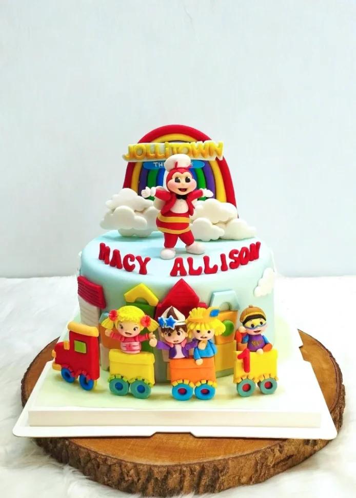 Jollitown themed birthday cake with Jollibee, Hetty, Popo, Yum, and Twirlie figures on a light blue fondant base with a rainbow.