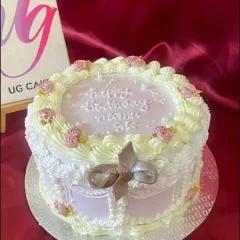 A round lavender minimalist cake with white piped borders, pink icing rosettes, and a brown gumpaste bow on the side.