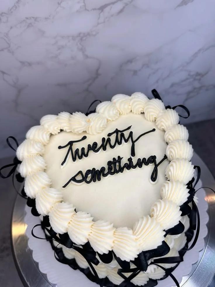Heart-shaped white minimalist cake with black piped icing text and black satin ribbons around the sides.