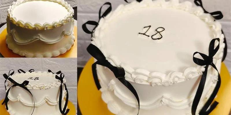 White minimalist cake with black satin ribbons and piped icing borders featuring the number 18 on top.