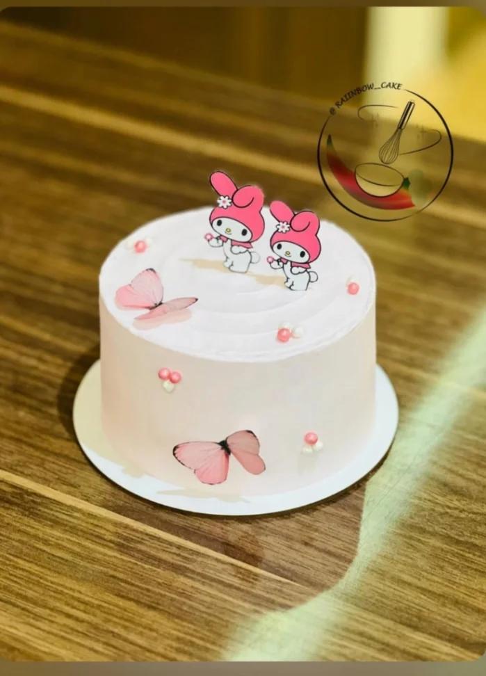 Light pink single tier My Melody cake with printed character toppers, pink butterflies, and white and pink icing dollops.