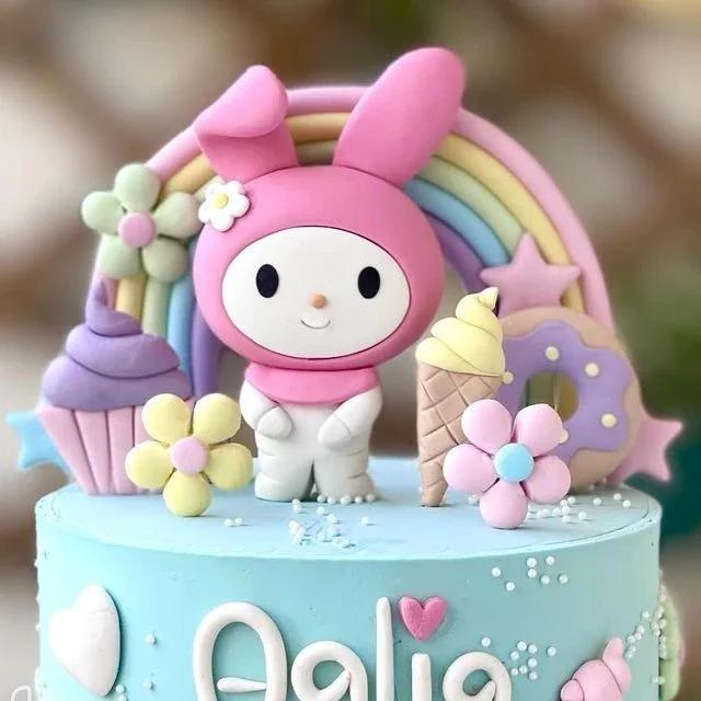 Light blue My Melody themed cake with a large pink fondant character, rainbow, cupcake, and donut toppers.